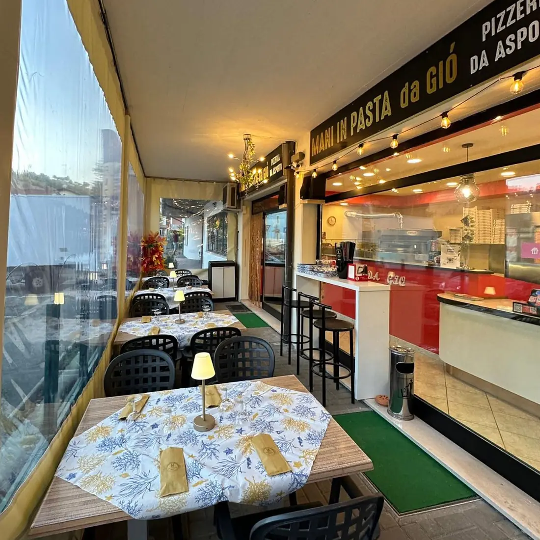 La veranda con i tavoli apparecchiati e l'insegna Mani in Pasta da Giò
